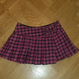 Rutig kortkjol med bältesdetaljer - Snygg kortkjol i rosa och svart rutigt mönster med två bältesdetaljer framtill. Perfekt för en trendig look!