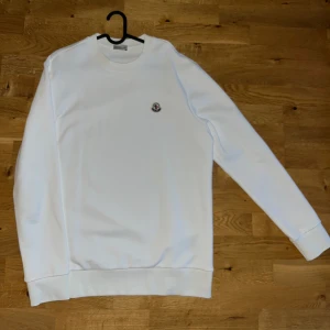 Vit tröja från Moncler - Passar dig som är 180-190 cm. Säljer en stilren vit tröja från Moncler med rund hals och långärmade ärmar. Tröjan har en diskret Moncler-logga på bröstet. Perfekt för en minimalistisk look.
