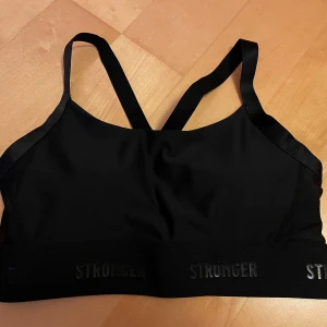 Sporttopp, strl S från Stronger - Svart sporttopp från Stronger, strl S. Justerbara axelband som korsas i ryggen. Brett resårband nedertill med logotypen 'STRONGER'. Helt ny.