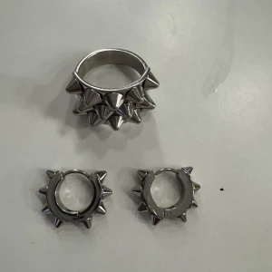 Silvriga ringar med nitar från Edlad - Ringen=300 örhängen=200kr kan köpa båda och kostar då 500 istället för 600,Pris går att diskutera.Säljer ett set med silvriga ringar från Edlad, dekorerade med coola nitar. Perfekt för att ge din stil en edgy touch. Ringarna har en robust design och är tillverkade i metall.