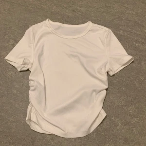 Vit ribbad t-shirt - Säljer en stilren vit ribbad t-shirt med korta ärmar. Perfekt för en enkel och avslappnad look. T-shirten har en rund halsringning och är tillverkad i ett mjukt material.