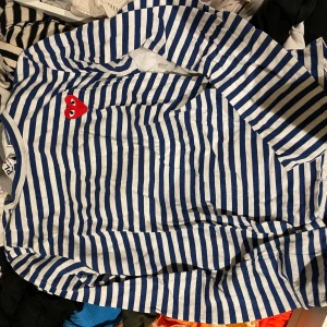 Randig tröja från Comme des Garçons - Säljer en randig långärmad tröja från Comme des Garçons med blå och vita ränder. Tröjan har ett rött hjärta broderat på bröstet. Perfekt för en stilren och avslappnad look.