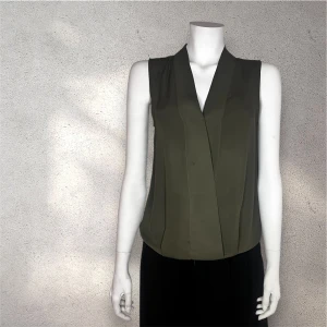 Olivgrön ärmlös blus Gina Tricot - Snygg olivgrön ärmlös blus från Gina Tricot  med omlott-design. Perfekt för en stilren look. Blusen har en djup v-ringning och är tillverkad i ett mjukt material som ger en bekväm passform.