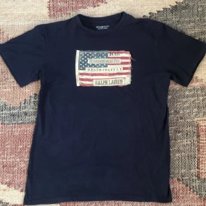 Ralph Lauren Denim&Supply t-shirt - En otroligt elegant och stilren t-shirt med ett tryck med en USA flagga med en sliten design. Ett bra bra skick lite använt men inga hål eller liknande. Sitter lite mindre än vad storleken säger. Hör av dig vid eventuella frågor eller funderingar!