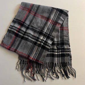 Grå rutig scarf från Burberry - Säljer en stilren grå rutig halsduk från Burberry, tillverkad i 100% lammull. Använd några få gånger men ändå nyskick. 