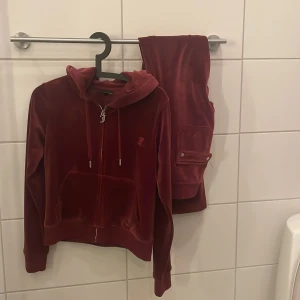 Vinröd hoodie och byxor från Juicy Couture - Säljer en snygg vinröd hoodie och matchande byxor från Juicy Couture. Hoodien har dragkedja med ett J-hänge och byxorna har praktiska fickor. Perfekt för en avslappnad och stilren look. Nypris 1200