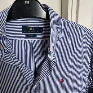 Randig skjorta - Ralph Lauren - Blå- och vitrandig skjorta från Ralph Lauren. Skick: 9/10, väldigt fint skick. Storlek: M, slim fit. Kontakta SOS för fler bilder eller info!