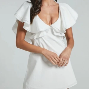 Studentklänning - Säljer en superfin vit klänning med stora volangdetaljer och öppen rygg. Klänningen har en v-ringad design och knytband i nacken. Perfekt till sommaren eller studenten