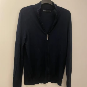 Mörkblå kofta från S.C.W. - Säljer en stilren mörkblå kofta från S.C.W. med dragkedja framtill. Perfekt för lager-på-lager och har långa ärmar. Passar bra till både vardag och mer uppklädda tillfällen. Skriv om ni har funderingar och priset är inte hugget i sten!