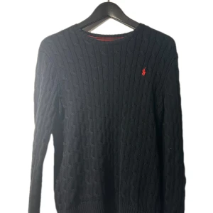 Svart stickad tröja från Ralph Lauren - Säljer en stilren svart stickad tröja från Ralph Lauren med det klassiska röda logotypen på bröstet. Tröjan har en rund halsringning och långa ärmar, perfekt för kyligare dagar. Passar både till vardags och mer uppklädda tillfällen. 