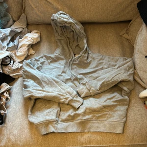 Grå hoodie - Säljer en bekväm grå hoodie med justerbar huva och känguruficka framtill. Perfekt för en avslappnad stil. Passar bra till jeans eller mjukisbyxor. ”Boxig” passform. Hör av dig vid intresse!