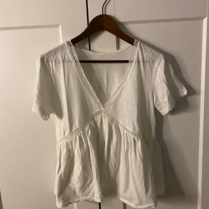 Vit blus med spetsdetaljer - Säljer en söt vit blus med v-ringning och spetsdetaljer. Blusen har korta ärmar och en luftig passform med rynkad nederdel. Perfekt för en avslappnad och stilren look. Lappen saknas och vet då inte vilket märke det är 💞