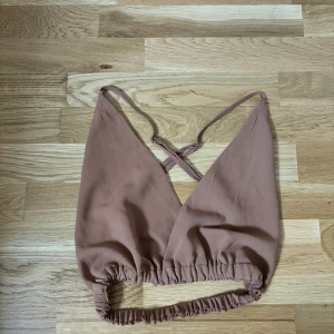 Brun omlott topp - Säljer en snygg brun omlott topp med smala axelband och elastisk nederkant. Perfekt för varma dagar eller som ett lager under en jacka. Toppen har en stilren design med korsade band i ryggen.