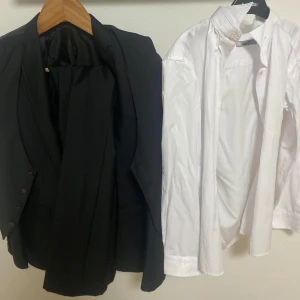 Kostym full set för 12 åringar - Elegant svart kostym med kavaj och byxor, perfekt för formella tillfällen. Kavajen har en klassisk design med knappar och fickor. Den vita skjortan är stilren och passar utmärkt till kostymen. Det ingår också en väst som passar perfekt till kavajen.                                        Storleken är till 12 åringar.