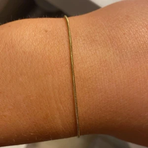 Tunt guldarmband - Elegant och minimalistiskt guldarmband med en tunn kedja. Perfekt för en subtil och stilren look. Passar bra att bära både ensam eller tillsammans med andra smycken för en lager-på-lager-effekt.