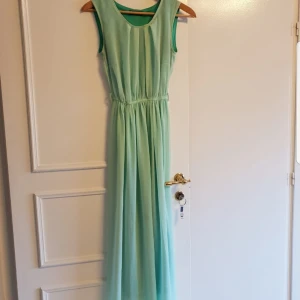 Mintgrön ärmlös långklänning - Elegant mintgrön långklänning med rund hals och ärmlös design. Perfekt för sommarens festligheter med sin luftiga och lätta känsla. Klänningen har en smickrande passform med elastisk midja för extra komfort. För barn. 164/170