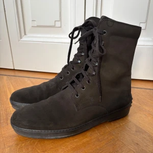 Bruna boots / herrstövlar från Tod's, storlek 9,5 (44) - Snygga svarta boots / herrstövlar från Tod's i mocka med snörning och en unik sula med gummiknoppar. Perfekta för en stilren look. Utmärkt skick, storlek 9,5 - 44. Liknar Hogan, Gucci, Santoni, Fratelli Rossetti.