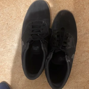 Svarta Nike sneakers - Säljer ett par svarta Nike sneakers med grå swoosh och bruna sulor. Skorna har snörning och är perfekta för vardagsbruk.