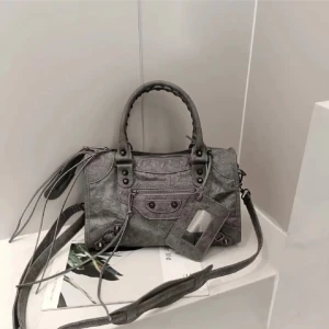 Grå handväska med dragkedja - Snygg grå handväska i syntetmaterial med flätat handtag och avtagbar axelrem. Väskan har flera dragkedjor och knappar för extra stil och funktionalitet. Perfekt för att bära dina dagliga nödvändigheter. Ny skick! Kom privat för fler bilder💗