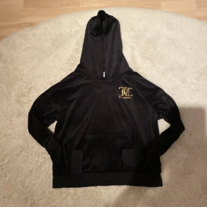 Svart hoodie från Juicy Couture - Säljer en snygg svart hoodie från Juicy Couture med guldtryck på bröstet. Den har en klassisk huva och en bekväm passform. Perfekt för en avslappnad stil.
