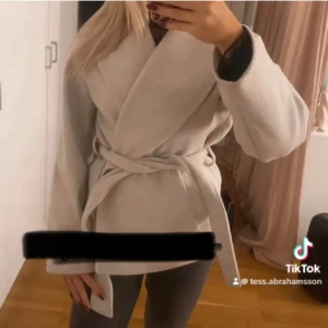 Kappa  - Snygg  kappa med knytband i midjan. Perfekt för en stilren look. Långärmad design med en elegant omlottstil.