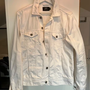 Vit jeansjacka från Dr. Denim - Säljer en stilren vit jeansjacka från Dr. Denim. Jackan har knappar framtill och två bröstfickor med knappstängning. Perfekt för en avslappnad look.