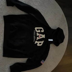 Svart hoodie från GAP - Säljer en svart hoodie från GAP med texten 'GAP Times Square' på framsidan. Säljes pågrund av att den är för stor  (STORLEK MEDIUM) Aldrig använd, bara provad snabb. Priset är inte hugget i sten