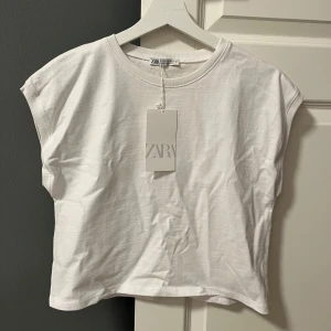 Vit T-shirt från Zara - Säljer en enkel och stilren vit T-shirt från Zara. Den har en rund halsringning korta ärmar. T-shirten är i ett mjukt bomullsmaterial. 