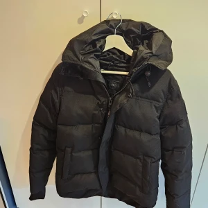 Canada Goose Macmillan Black Label - Säljer en svart parkajacka från canada goose med huva och dragkedja. Jackan är perfekt för kalla dagar och har en stilren design med långa ärmar och praktiska fickor. Passar bra för vintersäsongen. Storlek S, jätte fint skick. 
