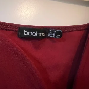 Vinröd klänning från Boohoo - Elegant vinröd klänning från Boohoo med långa puffärmar och en smickrande v-ringning. Perfekt för en stilfull kväll.