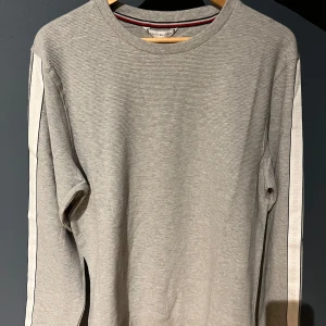 Tröja Tommy Hilfiger - Snygg grå tröja från Tommy Hilfiger. Tröjan är storlek M och gjord av 100% bomull. Orginal pris är 999kr på Boozt, där den är köpt ifrån. Aldrig använts och taggarna är kvar. Bara att fråga om du funderar på något!