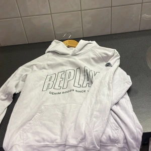 Vit hoodie från Replay - Säljer en vit hoodie från Replay med tryck på framsidan och en liten logga på ärmen. Perfekt för en avslappnad stil. Den har en klassisk huva och en bekväm passform.