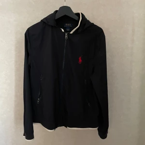 Svart jacka från Polo Ralph Lauren - Säljer denna snygga svarta ”windbreaker” jacka från Ralph Lauren. Jackan har inga defekter förutom att sömmarna gått sönder, ( se bild 2 ). Jackan passar någon som bär storlek S. Kvitto medföljer men pga defekten på andra bilden är jackan billigare. Skriv om ni har fler frågor🙌🙌