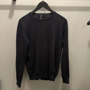 Stickad tröja från H&M - Säljer en stilren mörkblå tröja från H&M i storlek M. Tröjan har en klassisk design med långa ärmar och rund halsringning. Perfekt för en minimalistisk look.