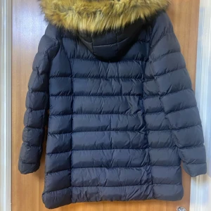 Svart dunjacka med fuskpäls från polo club - Snygg svart dunjacka med fuskpäls på huvan. Jackan har dragkedja och knappar framtill samt praktiska fickor med dragkedjor. Perfekt för kalla dagar.