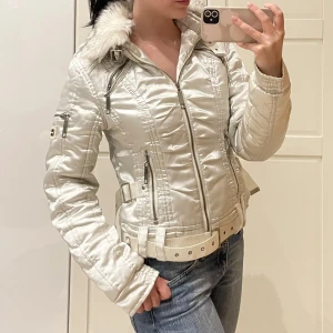Vit jacka med pälsdetaljer😻 - Snygg vit y2k-jacka med quiltad design och pälsdetaljer på huvan (pälsen sitter med vanliga knappar så går att ta bort)🤩har bälte i midjan för en tight passform som går att justera!! Märkt som strl L men skulle sitta bäst på en S-M beroende på hur tajt man vill att passformen ska vara. Men jag är XS-S och den sitter ju supersnyggt också❤️Inga uppenbara defekter. Tyget är lite silkesaktigt därför ser den gråfläckig ut men den är helt vit