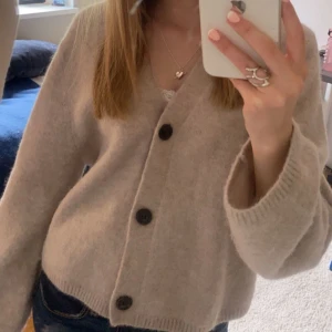 Beige kofta från other stories - Mysig beige kofta från Other stories med stora knappar framtill. Den har en v-ringad design och långa ärmar, perfekt för kyligare dagar. Koftan är tillverkad i ett mjukt material som ger en avslappnad och bekväm passform. Nypris 690kr