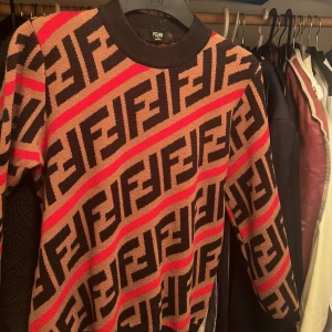 Mönstrad tröja från Fendi - Snygg tröja från Fendi med ett iögonfallande mönster i svart, röd och beige. Tröjan har långa ärmar och en rund halsringning. Perfekt för att sticka ut i mängden!. 