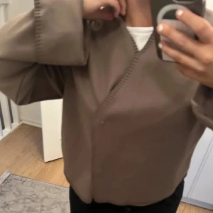 Beige jacka med omlott-design - Säljer en stilren beige jacka med omlott-design och långa ärmar. Perfekt för en chic och avslappnad look. Jackan har en enkel och elegant stil som passar till många olika outfits.