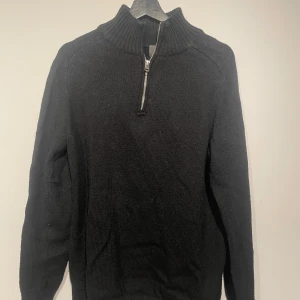 Svart stickad tröja från H&M - Snygg svart stickad tröja från H&M med dragkedja vid halsen. Perfekt för kyliga dagar med sin ribbade krage och långa ärmar. En stilren och bekväm tröja för alla tillfällen.