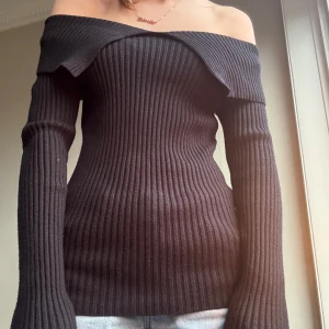 Svart offshoulder tröja - Snygg svart offshoulder tröja, som är lång i kroppen med lång ärm. Perfekt för en stilren look. Tröjan har en ribbad struktur som ger en skön passform.