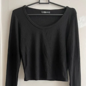 Svart ribbad tröja från FB Sister - Säljer en stilren svart ribbad tröja från FB Sister. Tröjan har långa ärmar och en rund halsringning, perfekt för en enkel och snygg look. Passar bra till både jeans och kjol.