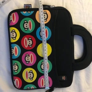 Paul Frank IPad Väska  - Säljer en cool datorväska med ett färgglatt mönster av apor i cirklar. Väskan har ett handtag och dragkedja för enkel användning. Perfekt för att bära din laptop med stil!