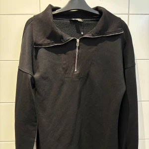 Svart tröja med dragkedja från Missguided - Snygg svart tröja från Missguided med en stilren dragkedja framtill. Tröjan har långa ärmar och en ribbad krage som ger en modern touch. Perfekt för en avslappnad look.