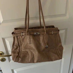 Beige axelväska med blommigt foder - Snygg beige handväska i med blommigt foder och spänne framtill. Perfekt för att bära med sig allt man behöver. Har några små defekter som inte är så märkbara