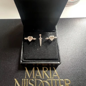Silverörhängen med hjärta och dolk från Maria Nilsdotter - Unika silverörhängen från Maria Nilsdotter med ett två hjärta och ett svärd. Perfekt för att ge en edgy touch till din stil. Kommer i en elegant svart ask. Ord pris är 4135kr. Säljer hjärt örhängena för 1199kr styck och 2300kr för båda. Säljer svärdet för 689kr. Köp alla för 2899kr. Fraktas samma dag som du köper.