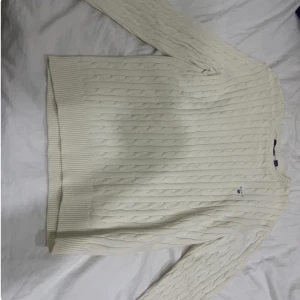 Vit stickad tröja från Gant - Säljer en stilren vit stickad tröja från Gant med kabelstickat mönster. Tröjan har långa ärmar och ribbstickade muddar vid ärmslut och nederkant. Perfekt för kyliga dagar! STORLEK: XS