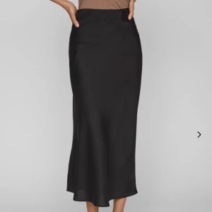 Svart långkjol från VILA - Elegant svart långkjol från VILA i ett mjukt och glansigt material. Kjolen har en klassisk och tidlös design som passar perfekt för olika tillfällen. Den är tillverkad i ett material som ger ett fint fall och en lyxig känsla. -Den är aldrig använd och har prislapp!💕