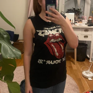 Svart ärmlös Rolling Stones topp från H&M - Säljer en cool svart ärmlös topp från H&M med Rolling Stones tryck fram och turnédatum bak. Perfekt för musikälskare som vill ha en rockig stil. Toppen är från H&M:s Divided-kollektion. Storleken är XS men passar mig som är M superbra🩷