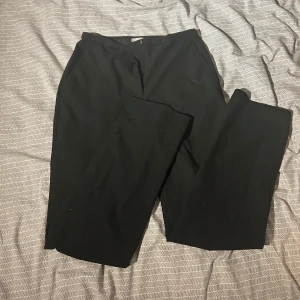 Svarta byxor från H&M - Säljer ett par stilrena svarta byxor från H&M. De har en klassisk design med rak passform och är perfekta för en elegant look. Byxorna är tillverkade i ett bekvämt material och har en midwaist skärning.